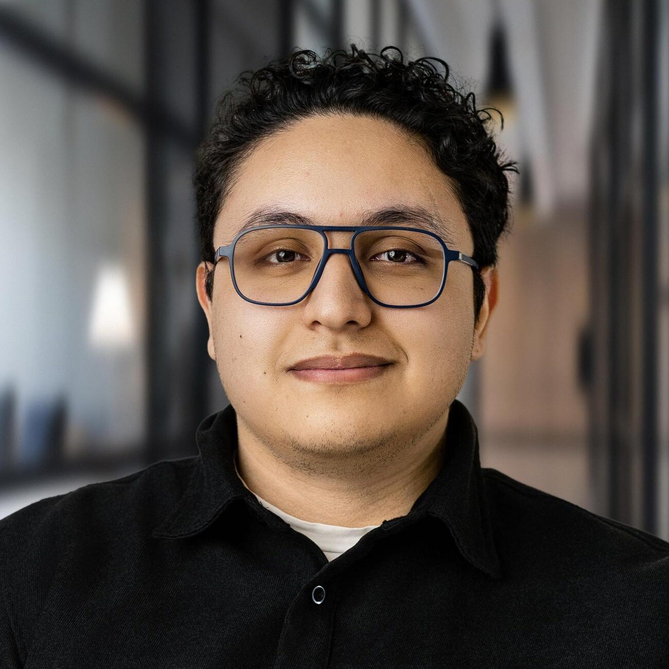 Membre de l'équipe portant des lunettes et une chemise noire, souriant dans un bureau.