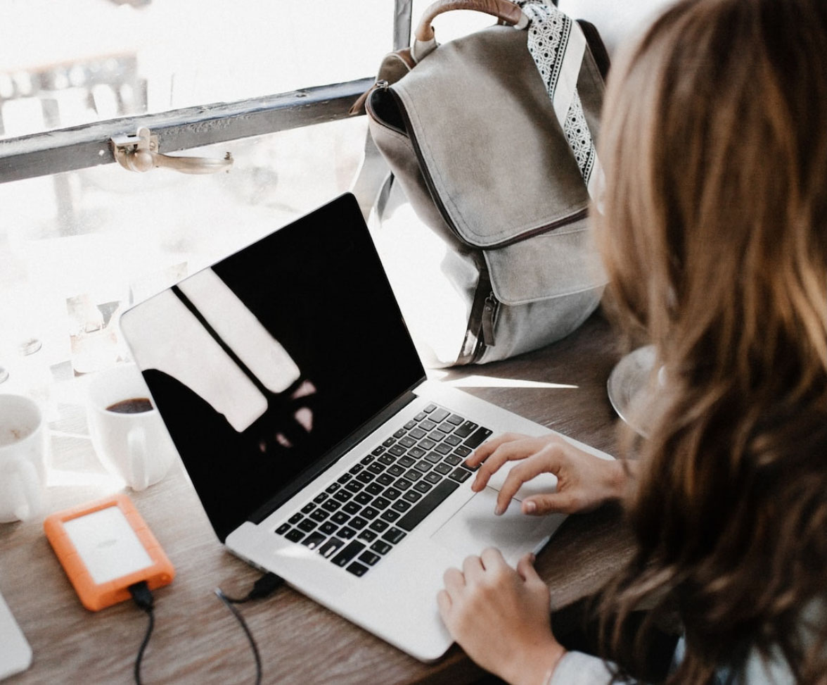 Personne travaillant sur un portable, avec disque dur externe, café et sac à dos