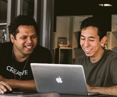 Deux collègues souriants regardent ensemble l'écran d'un ordinateur portable dans un bureau ouvert.